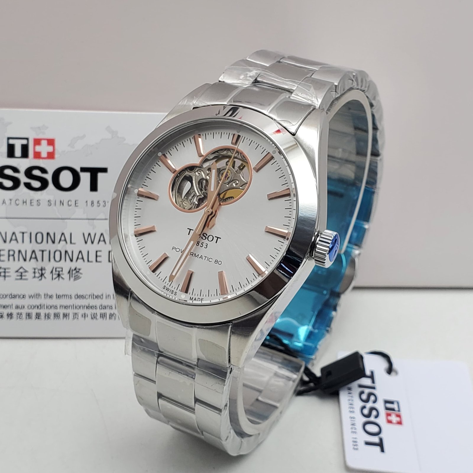 root A sleek Tissot watch with a silver band and white face, featuring a visible mechanical movement, displayed on a white background with its box and tag.