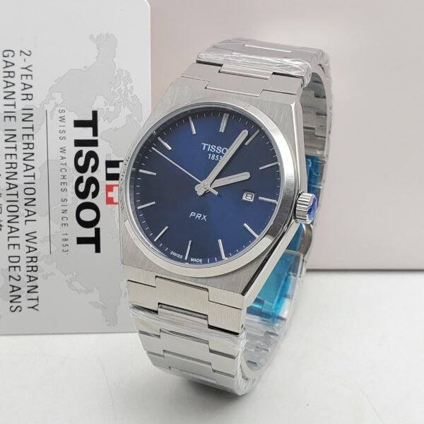 A sleek Tissot PRX watch with a blue face and silver metal band, presented with a 2-year international warranty card.