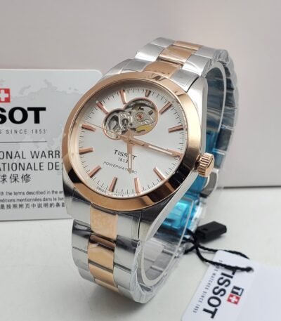 Tissot luxury watch with silver and rose gold band and white face, displayed on a white surface with its box and tag.