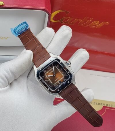A luxurious Cartier watch with a brown leather strap and silver case, featuring a brown dial with Roman numerals, held by a gloved hand with the Cartier box in the background.