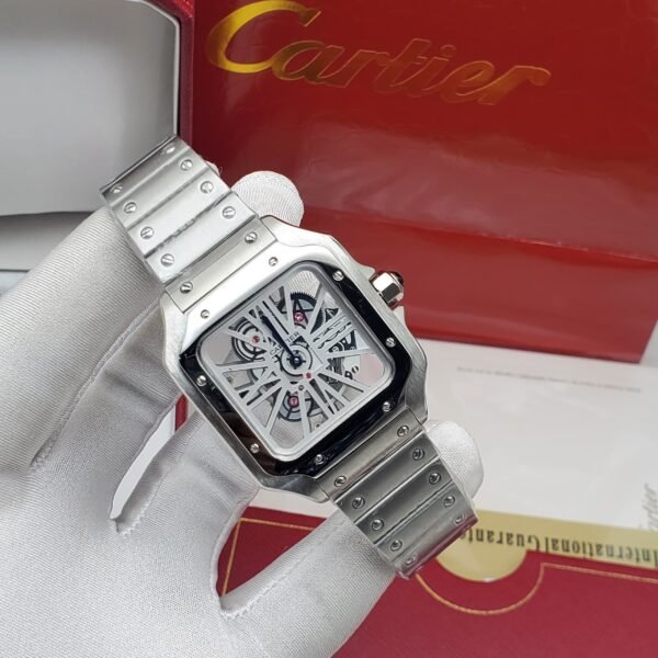 A luxurious silver Cartier watch with a sleek design and exposed mechanical components, presented on a white-gloved hand with the iconic red Cartier box in the background.