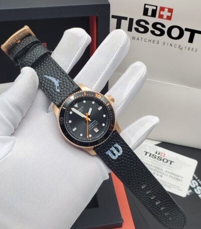 Tissot PRX Powermatic 80 watch with black leather strap and gold accents, presented on a white-gloved hand with box and warranty card in background.