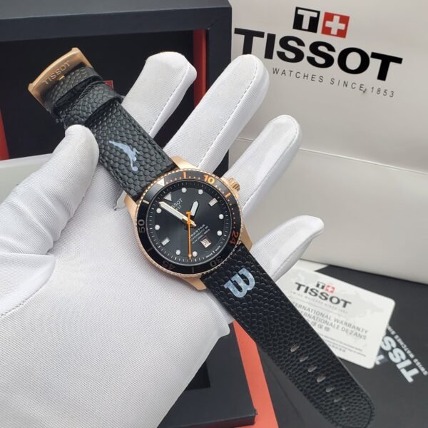 Tissot PRX Powermatic 80 watch with black leather strap and gold accents, presented on a white-gloved hand with box and warranty card in background.