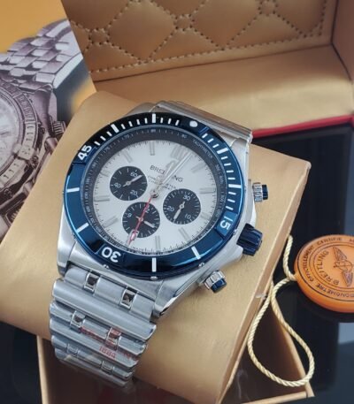 A luxurious silver watch with a white face and blue accents, nestled in a tan box with a red interior, exuding high-end quality and refinement.