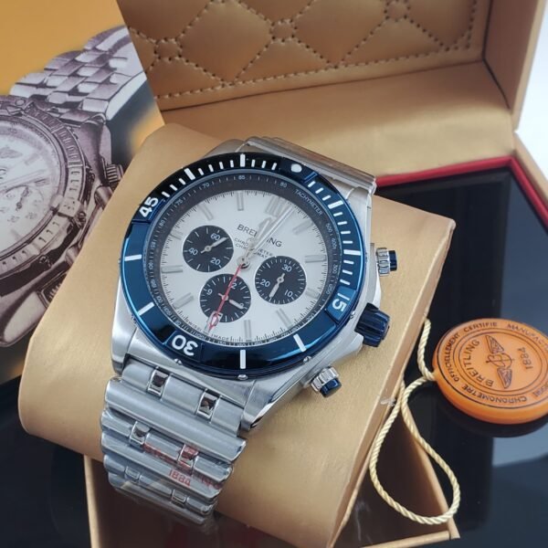 A luxurious silver watch with a white face and blue accents, nestled in a tan box with a red interior, exuding high-end quality and refinement.