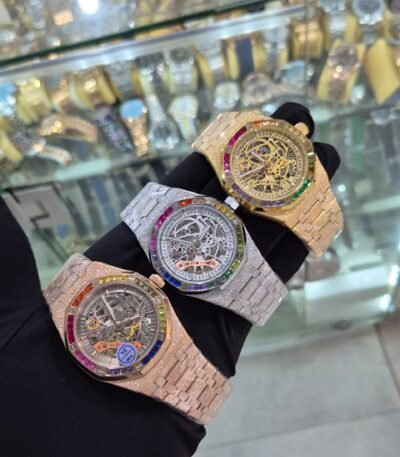 A hand showcasing three luxurious watches with rainbow gemstone bezels and intricate mechanical details.