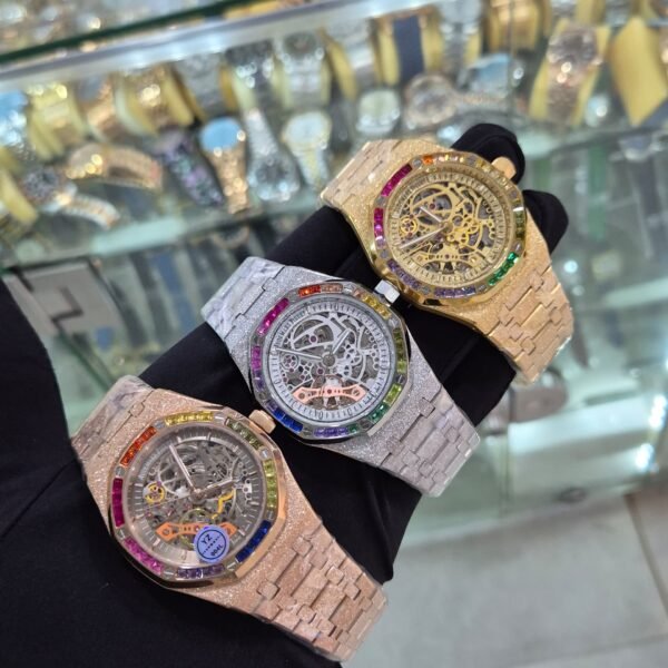 A hand showcasing three luxurious watches with rainbow gemstone bezels and intricate mechanical details.