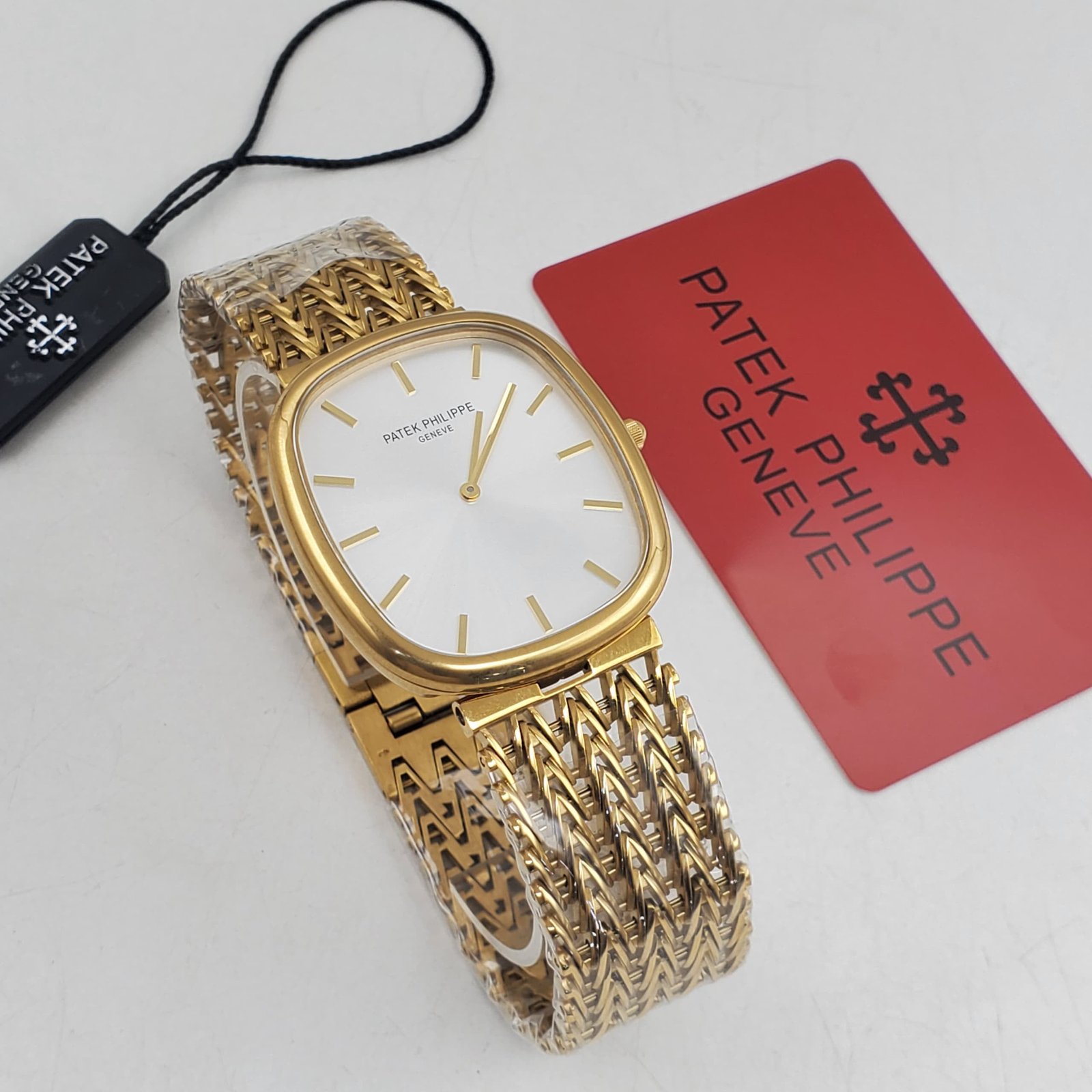 WhatsApp Image 2026-09-06 at 8.40fff.02 PM A luxurious Patek Philippe watch with a gold band and white face, accompanied by a red card and black tag, showcasing its high-end craftsmanship.