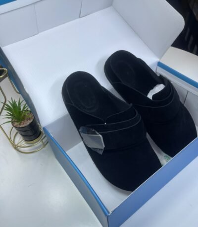 A pair of black velvet slides nestled in a white and blue shoe box, exuding luxury and comfort.