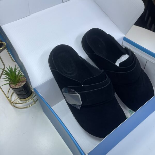 A pair of black velvet slides nestled in a white and blue shoe box, exuding luxury and comfort.