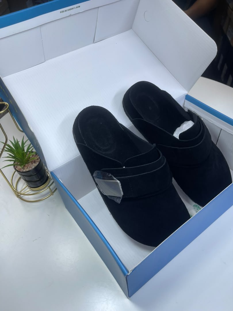 WhatsApp Image 2026-09-20 at 10.57.55 AM A pair of black velvet slides nestled in a white and blue shoe box, exuding luxury and comfort.