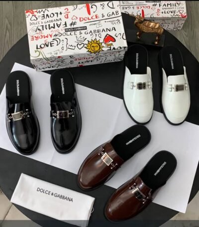 A stylish display of Dolce & Gabbana mule loafers in black, brown, and white, accompanied by their signature box and dust bag.