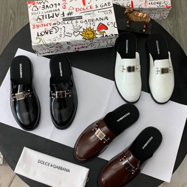 A stylish display of Dolce & Gabbana mule loafers in black, brown, and white, accompanied by their signature box and dust bag.